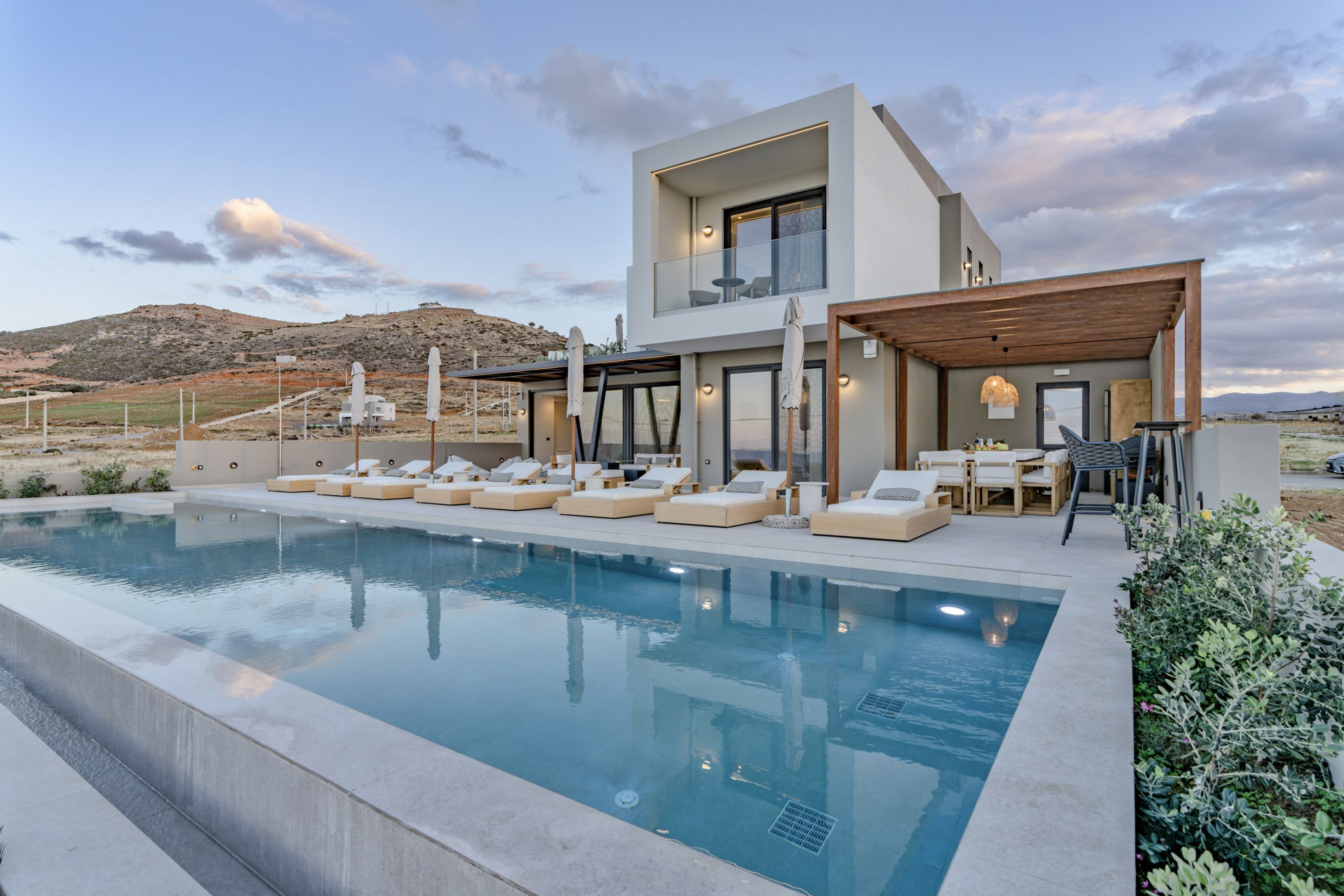 A modern two-story house with a swimming pool, outdoor seating, and a view of the hills.
