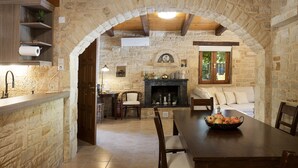 A rustic stone kitchen with a wooden dining table, a fireplace, and a cozy seating area. - Maratho Villa - With Private Pool (Rethymno)