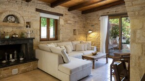 A cozy living room with a stone fireplace, a sofa set, and a dining area with a table and chairs. - Maratho Villa - With Private Pool (Rethymno)