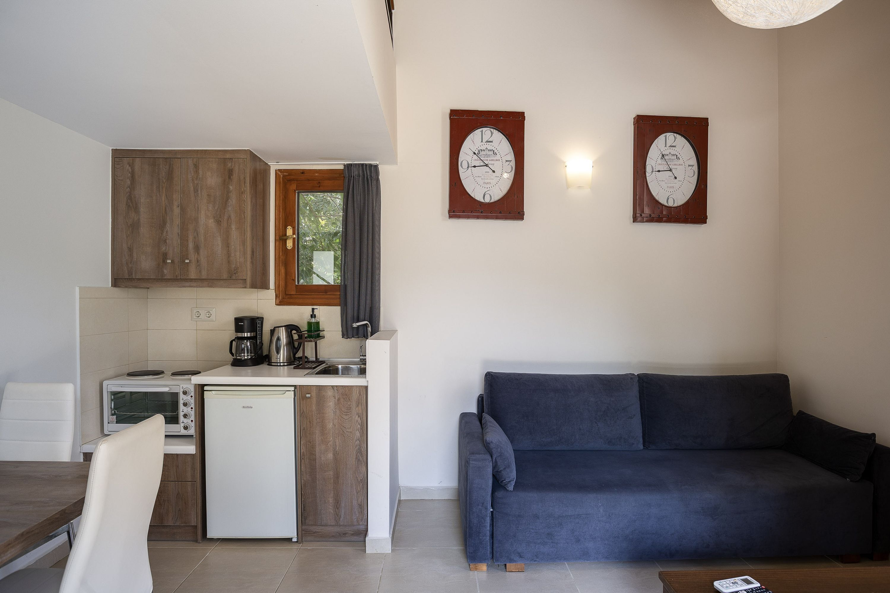 A compact living space with a kitchenette, a sofa, and two wall clocks.