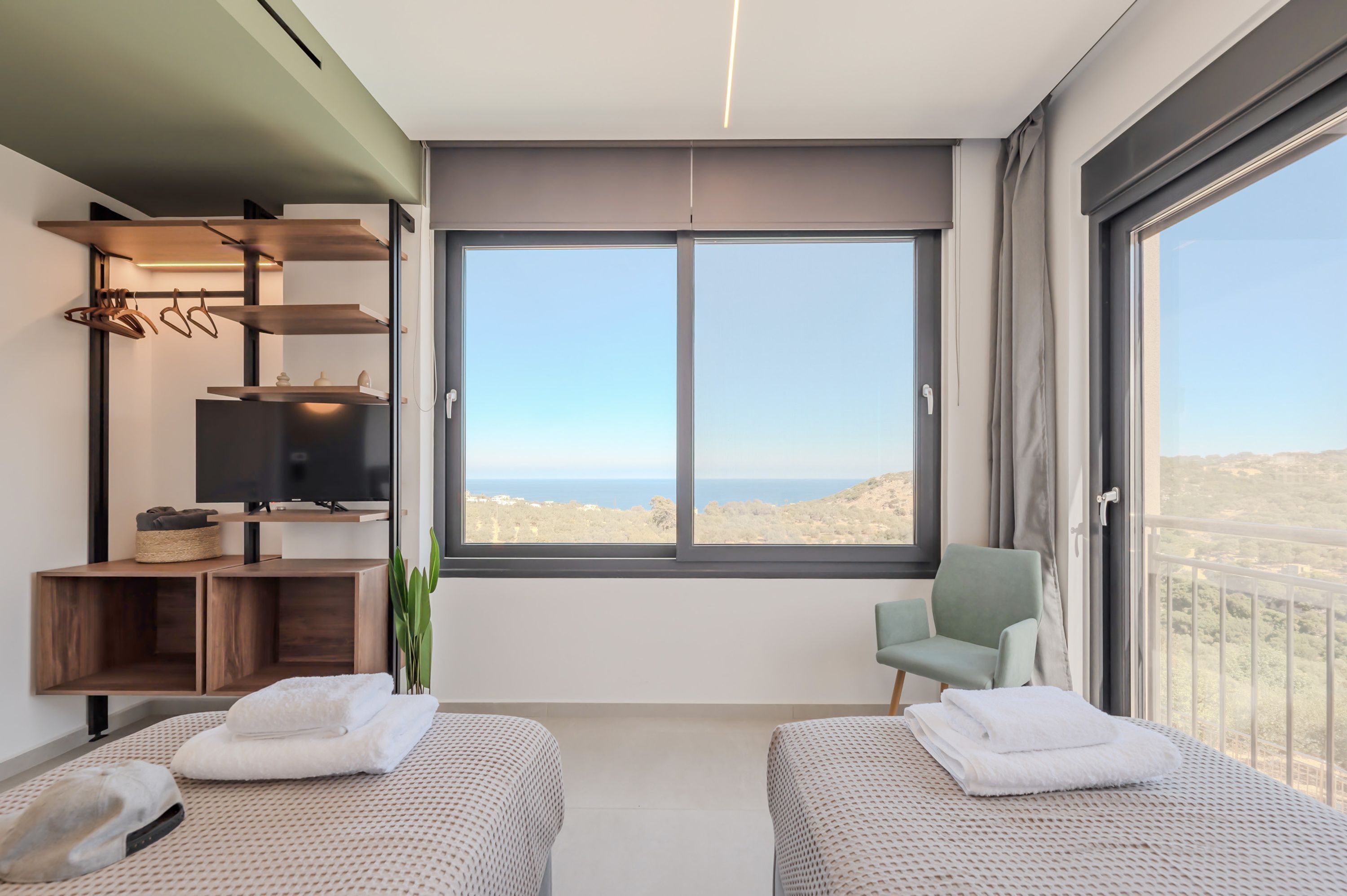 A modern hotel room with two beds, a TV, and a large window offering a view of the desert.