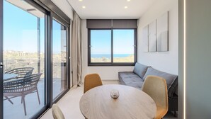 Una sala de estar moderna con un gran ventanal, una mesa redonda, un sofá y un balcón con mobiliario de mimbre.