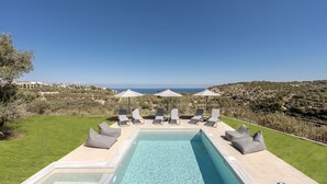 Piscina con sillas de descanso y sombrillas, rodeada de césped y con vistas a un paisaje montañoso.
