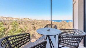 Un balcón con sillones de mimbre y una mesa, con vistas a un paisaje costero.
