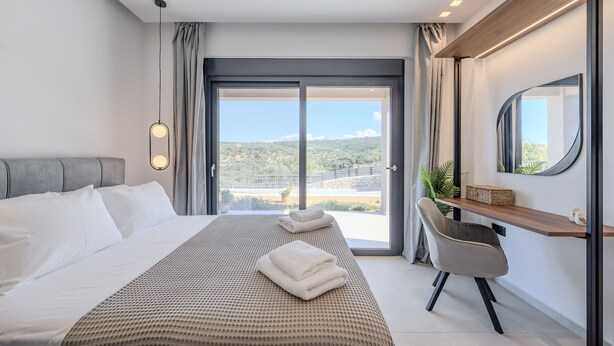 Habitación de hotel moderna con una cama grande, un escritorio y vistas a un paisaje verde a través de la puerta de cristal.