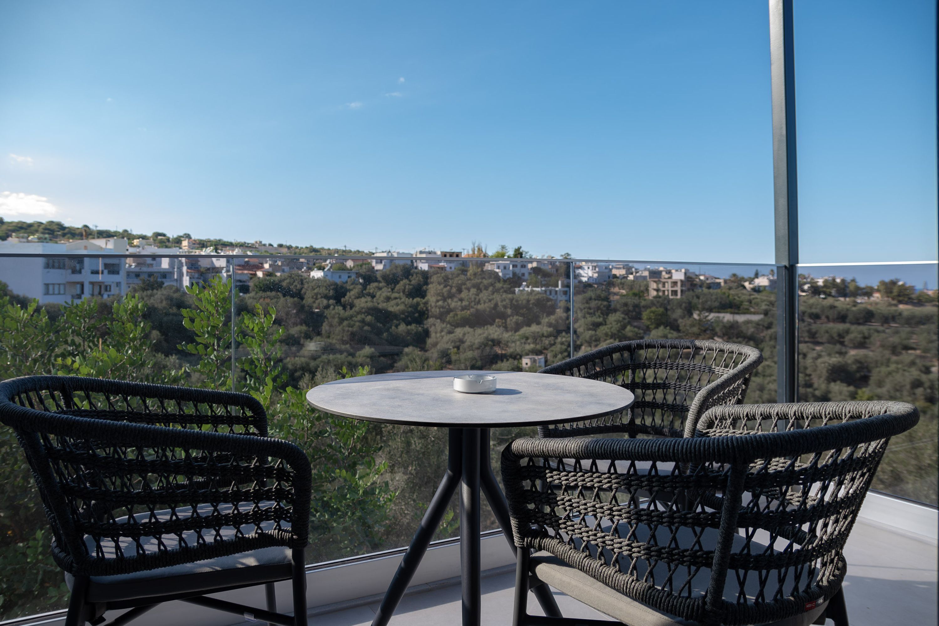 A balcony with wicker chairs and a small round table, overlooking a residential area and a body of water.