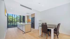 Una cocina moderna con una isla central, un área de comedor con mesa y sillas, y ventanas amplias con vistas a árboles.