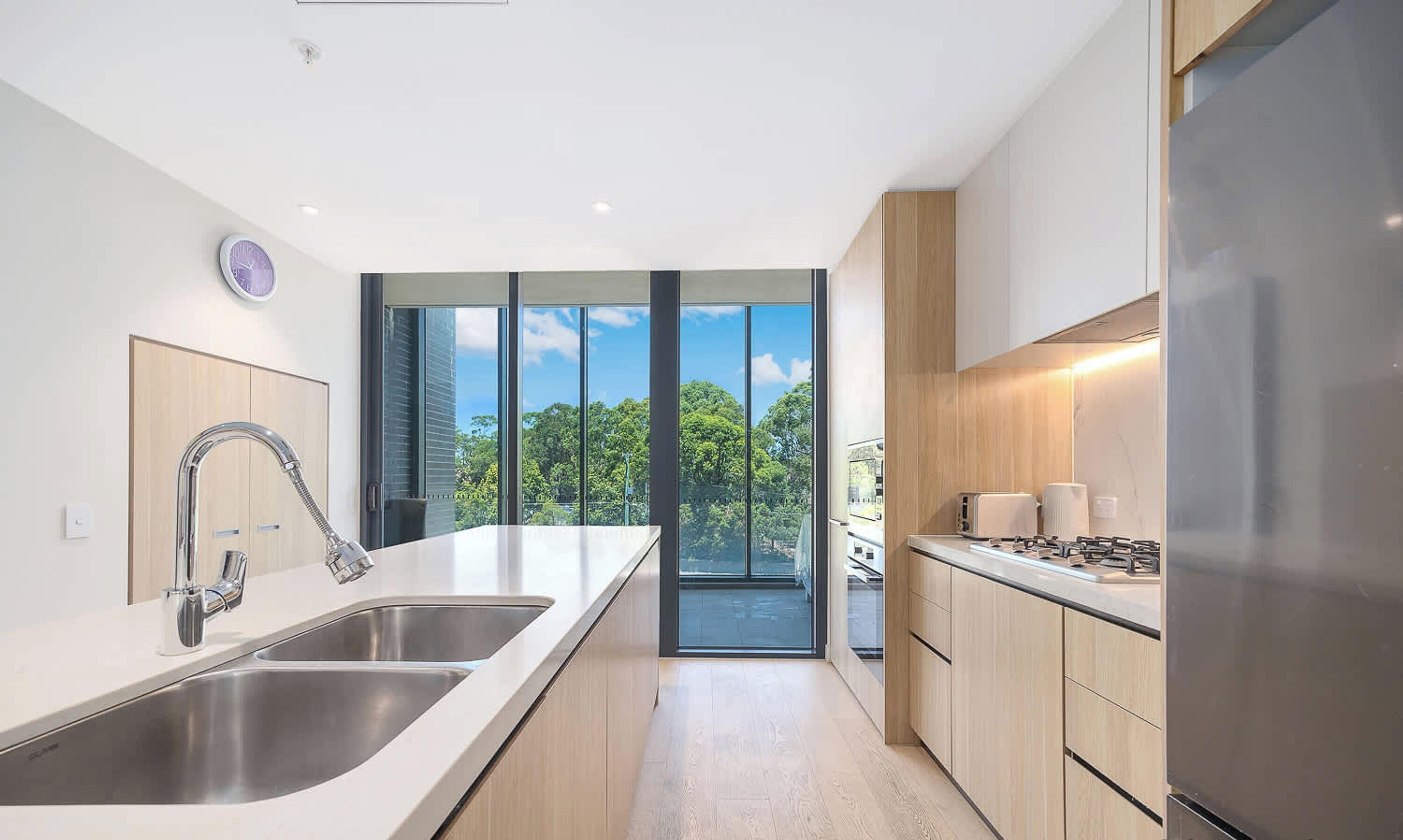 A modern kitchen with a large island, stainless steel appliances, and a view of trees through the windows.