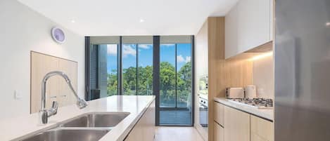 A modern kitchen with a large island, stainless steel appliances, and a view of trees through the windows.
