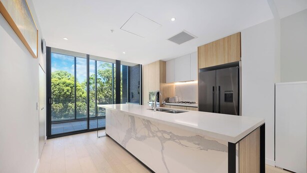 Una cocina moderna con encimera de mármol, electrodomésticos de acero inoxidable y amplias ventanas con vistas a zonas verdes.