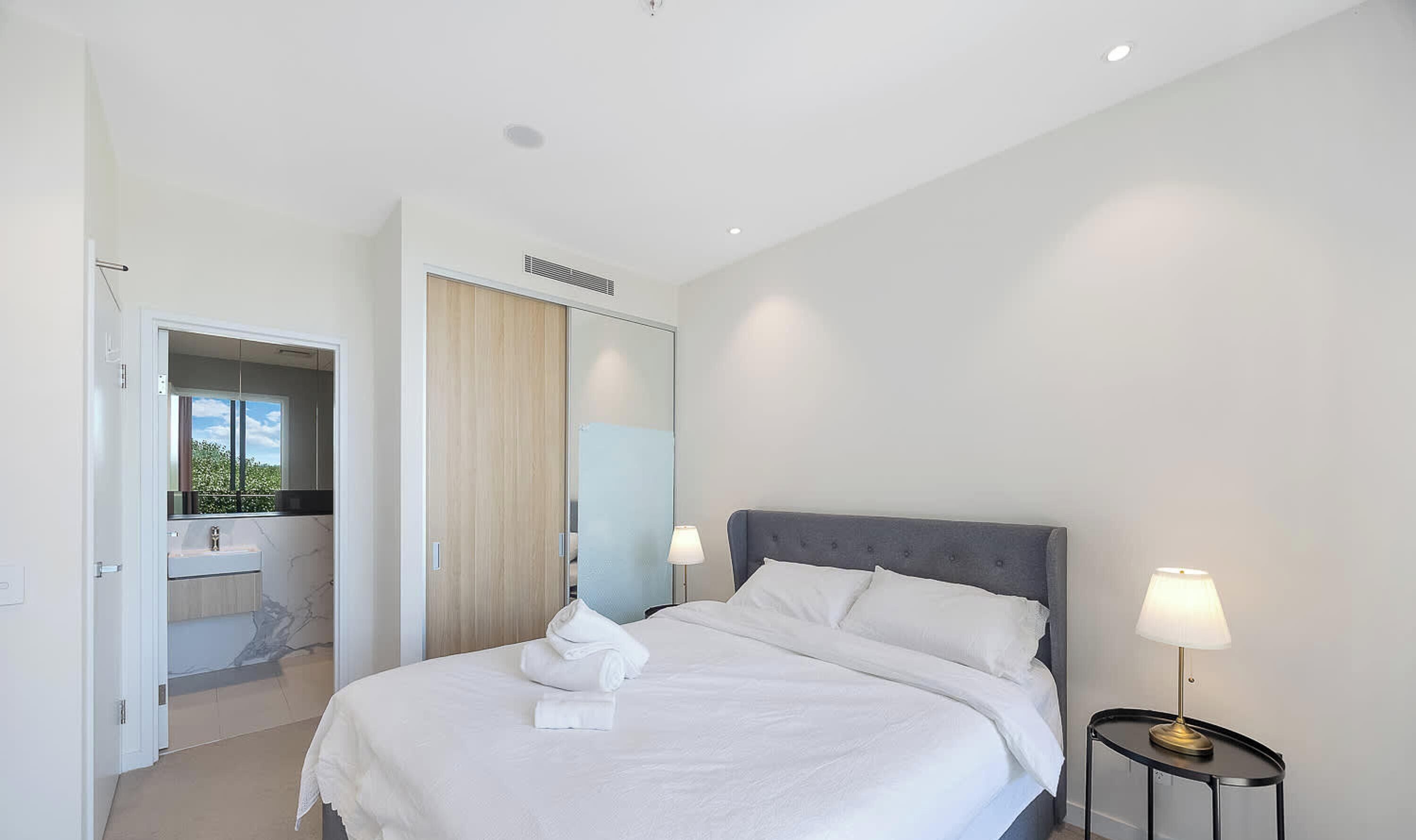 Ein Hotelzimmer mit Bett, Nachttisch mit Lampe, Badezimmer mit Spiegel und Blick ins Freie.