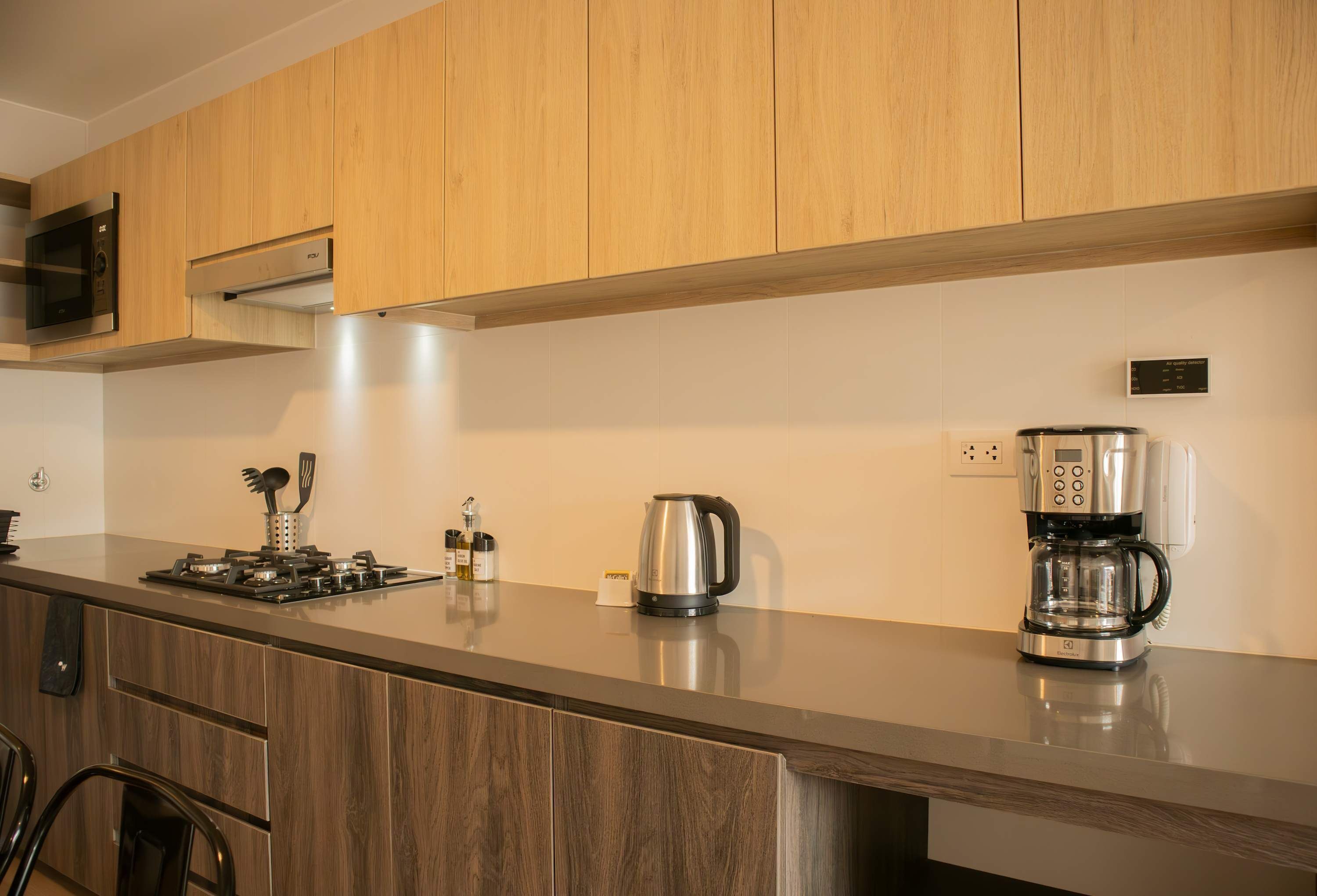 A modern kitchen with wooden cabinets, a stainless steel microwave, a kettle, and a coffee maker on the countertop.