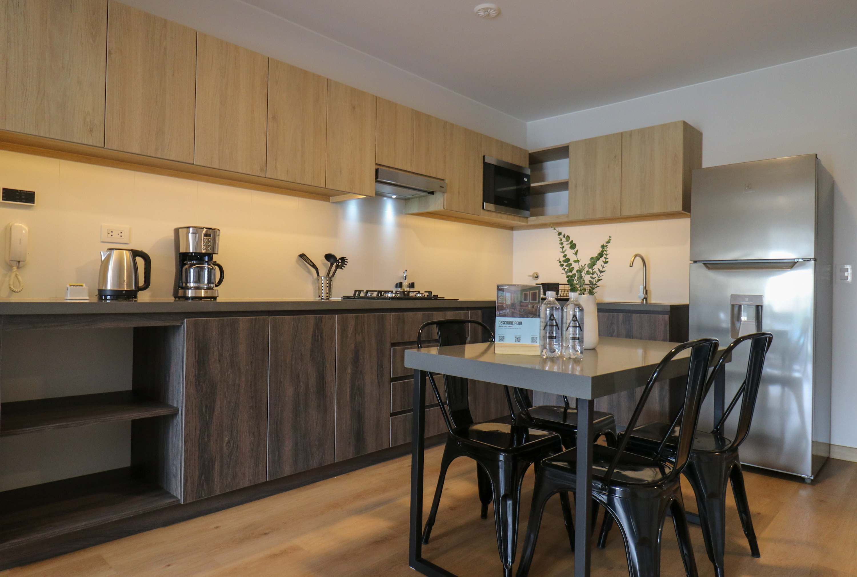 A modern kitchen with wooden cabinets, a stainless steel refrigerator, and a dining table with chairs.