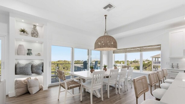 A spacious dining area with a large window, white furniture, and a hanging light fixture. - Ocean Views Beach Optional Heated Pool Spa (Palm Coast)