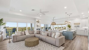 A spacious living area with a large L-shaped sofa, a round ottoman, and a view of the outdoors through large windows. - Ocean Views Beach Optional Heated Pool Spa (Palm Coast)