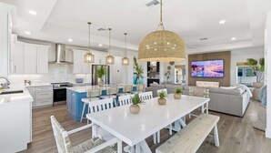 A modern kitchen with white cabinets, a large island, and a dining area with a white table and benches. - Ocean Views Beach Optional Heated Pool Spa (Palm Coast)
