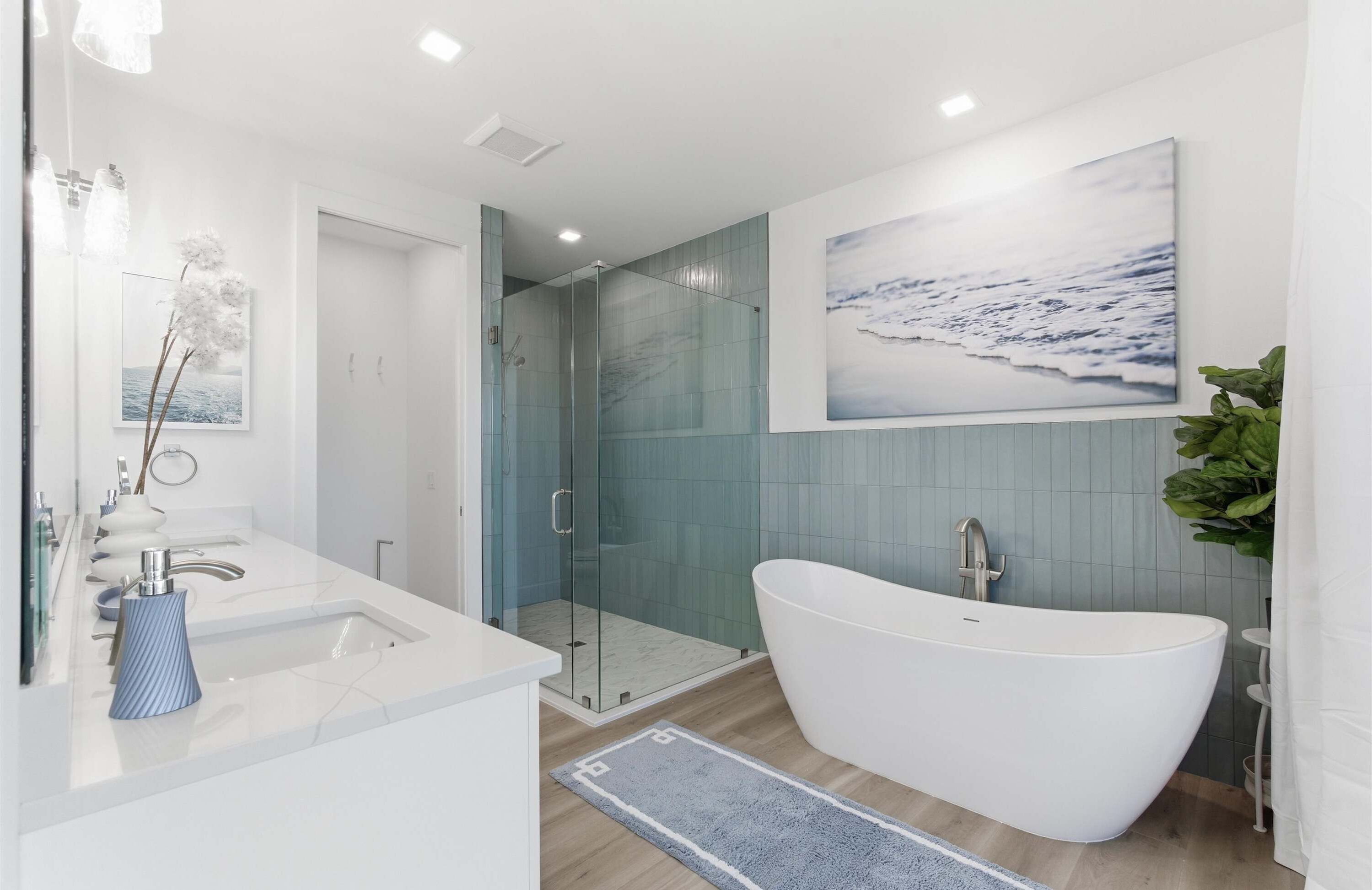 Un bagno moderno con una vasca freestanding, una doccia con pareti in vetro e un'ampia immagine appesa alla parete raffigurante una spiaggia.