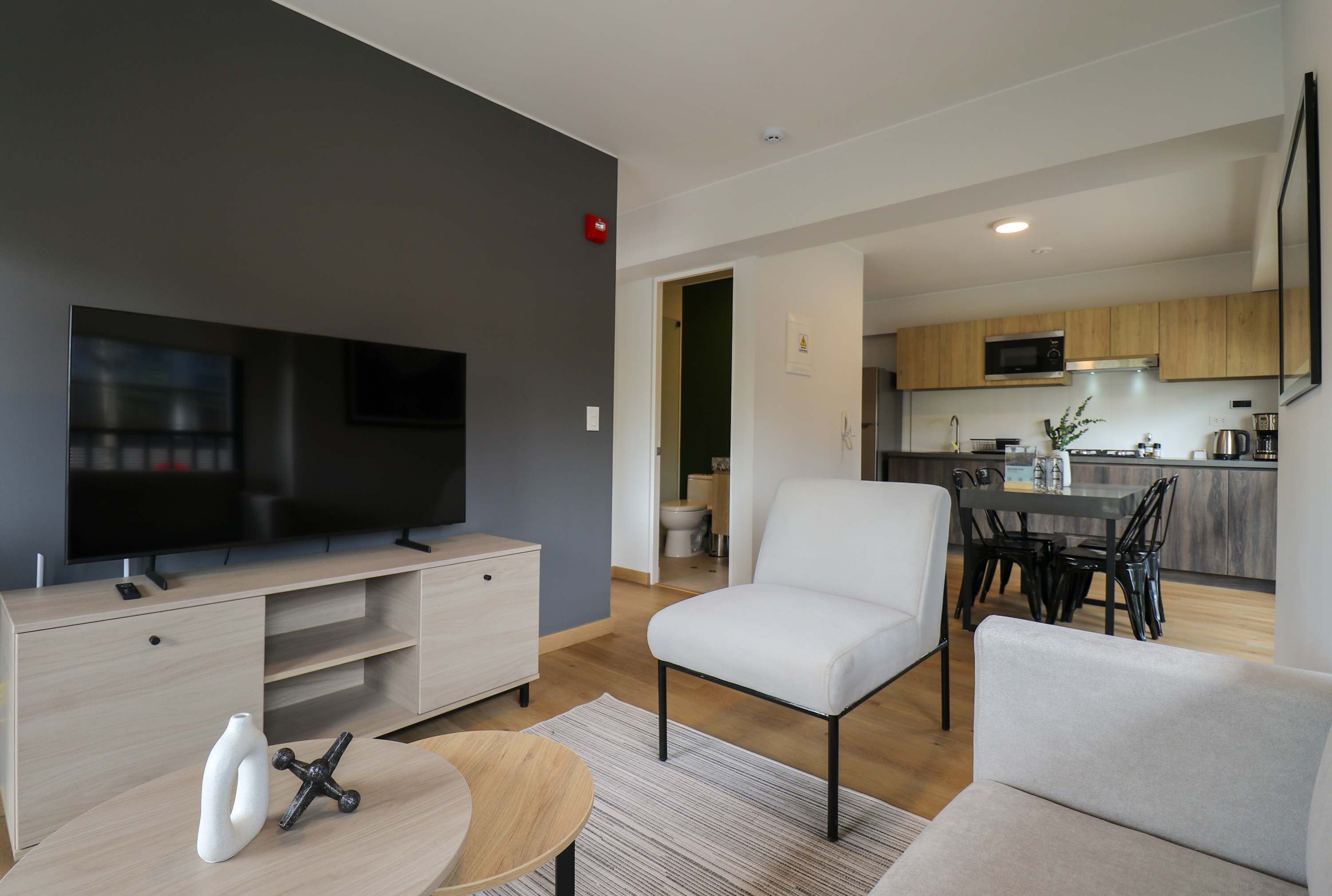 A modern living room with a flat-screen TV, a white sofa, and a dining area with a table and chairs.