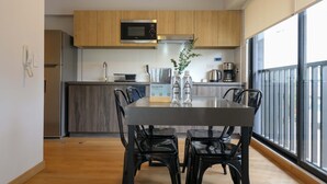 A modern kitchen with wooden cabinets, a stainless steel refrigerator, a microwave, and a coffee maker. There is a dining table with black chairs and a vase with green plants. - w Graceful 1BR w/ Perfect Balcony in Miraflores (Lima)