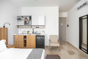 A modern hotel room with a bed, a wooden nightstand, a kitchenette with a coffee machine, a chair, and a sliding glass door leading to a bathroom. - w Engaging Loft in the Heart of Bocagrande (Cartagena)
