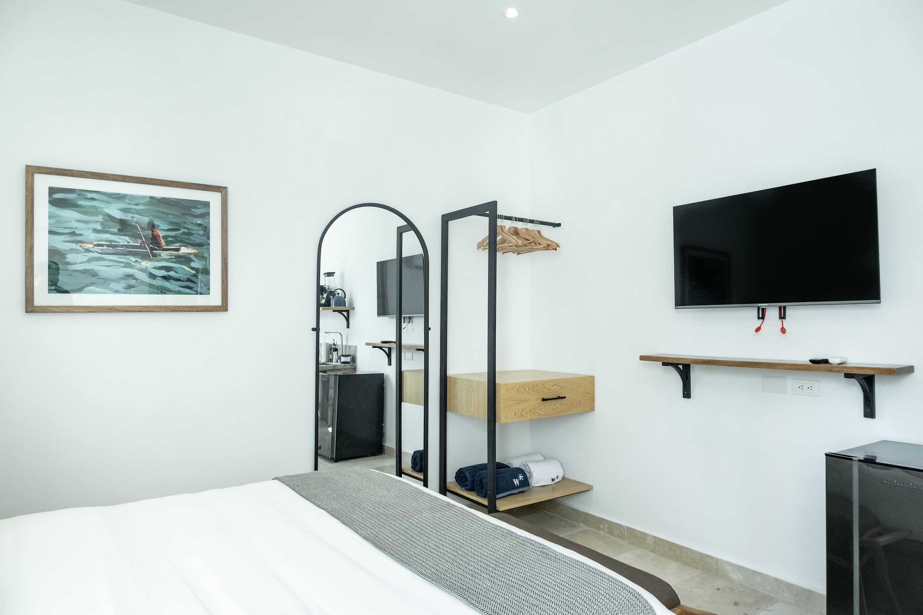 Ein modernes Hotelzimmer mit einem Bett, einem Fernseher, einem Spiegel, einem Holzregal und einem Bild an der Wand.