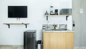 A compact kitchenette with a built-in refrigerator, microwave, and coffee maker on a shelf, a sink with a marble countertop, and a TV mounted on the wall. - w Upscale Loft in the Heart of Bocagrande (Cartagena)