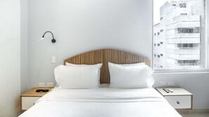 A minimalist hotel room with a wooden headboard, white bedding, a bedside table with a lamp, and a window with a city view. - w Signature Loft in the Heart of Bocagrande (Cartagena)