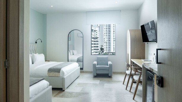 A modern hotel room with a bed, a desk, a chair, and a large window with a city view. - w Inviting Loft in the Heart of Bocagrande (Cartagena)