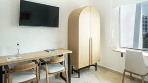 Ein modernes Zimmer mit einem Holzbüro, zwei Stühlen, einem an der Wand befestigten Fernseher und einem großen Schrank.