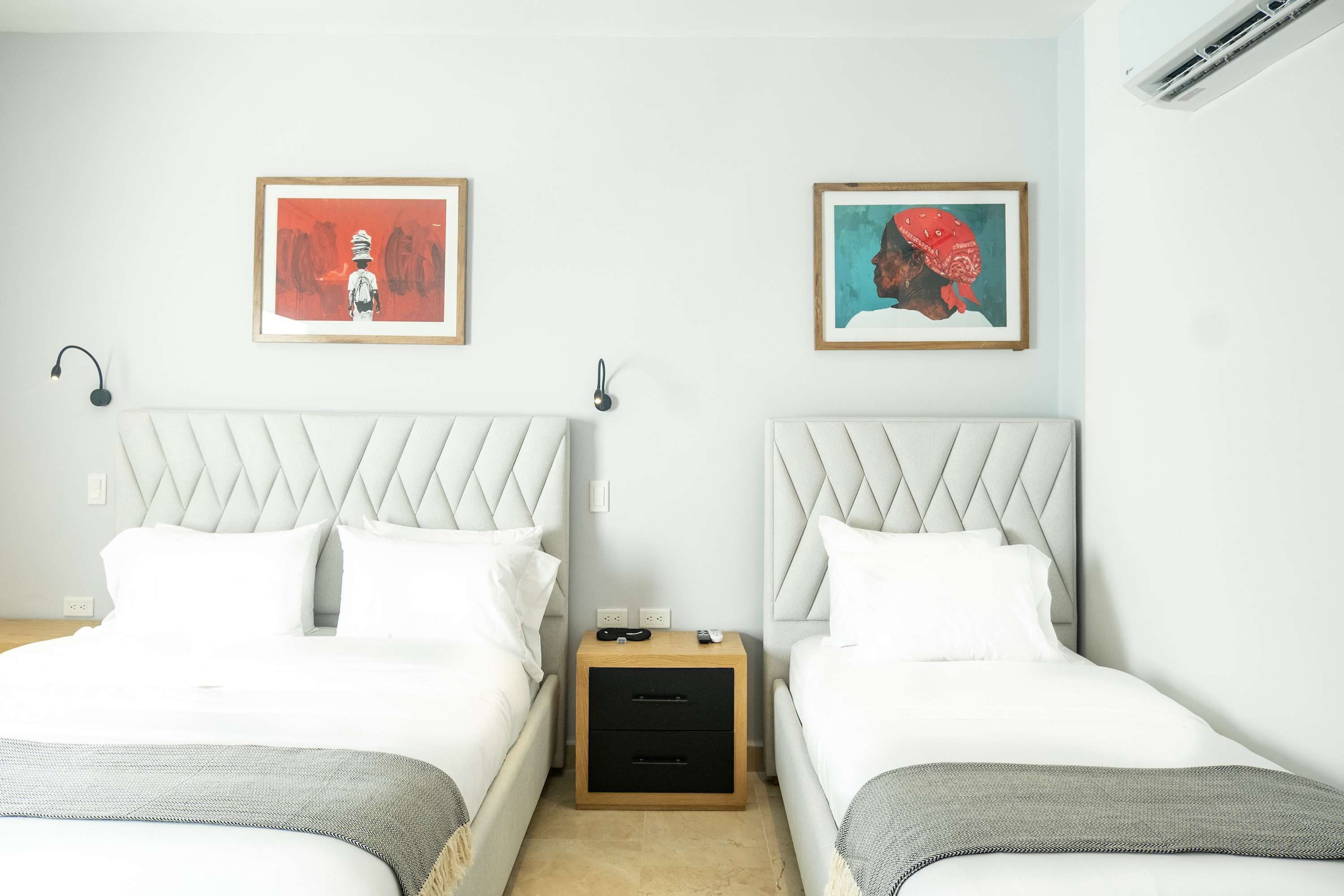 Una habitación de hotel con dos camas, una mesita de noche y dos cuadros enmarcados en las paredes.