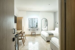 Een moderne hotelkamer met een bed, een bureau met stoel, een raam met uitzicht op de stad, en een badkamer met spiegel en wastafel.