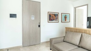 A room with a beige sofa, a wooden door, and two framed pictures on the wall. - w Trendy 2BR in the Heart of Bocagrande (Cartagena)