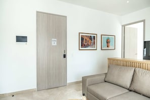 A room with a beige sofa, a wooden door, and two framed pictures on the wall. - w Trendy 2BR in the Heart of Bocagrande (Cartagena)