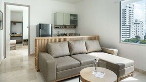 A modern living room with a sofa, a coffee table, and a TV. There is a kitchen area with cabinets and a microwave. The room has a large window with a city view. - w Trendy 2BR in the Heart of Bocagrande (Cartagena)