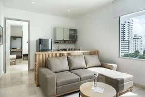 A modern living room with a sofa, a coffee table, and a TV. There is a kitchen area with cabinets and a microwave. The room has a large window with a city view. - w Trendy 2BR in the Heart of Bocagrande (Cartagena)