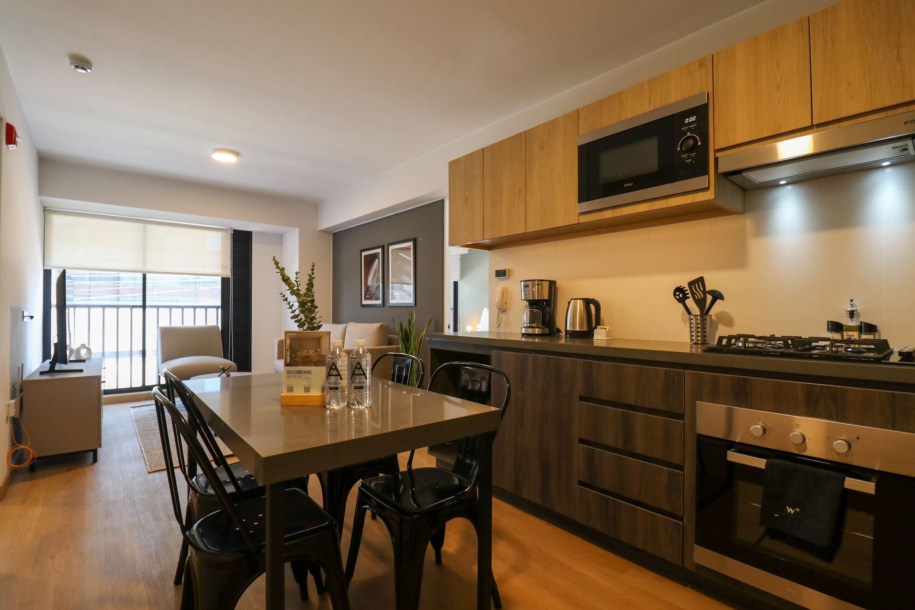 A modern kitchen with wooden cabinets, a microwave, a stove, and a dining area with a table and chairs.