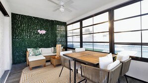 A modern room with a large window, a ceiling fan, a green wall, a wooden table, wicker chairs, and a patterned rug. - Spacious 4-bedroom house with golf, Pool, Sauna, Jacuzzi & Firepit (Largo)