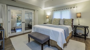 Un dormitorio con cama, banca, dos lámparas, ventilador de techo y vistas por una puerta corrediza.
