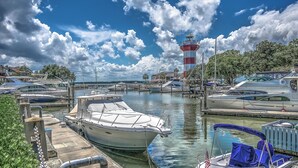Un puerto deportivo con barcos amarrados, un faro al fondo y cielo despejado.