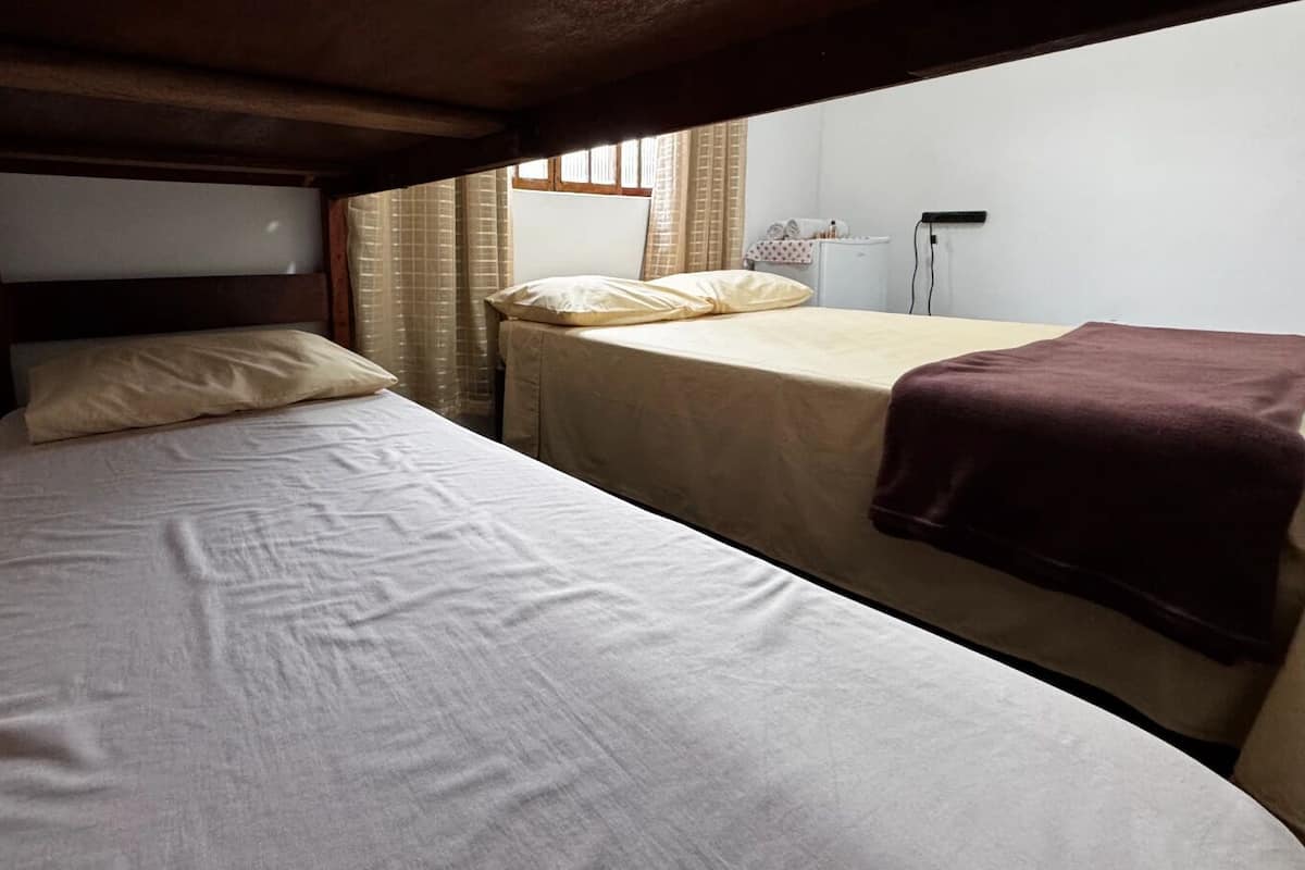 Una cama individual con cabecera de madera, una mesita de noche y una ventana con cortinas.