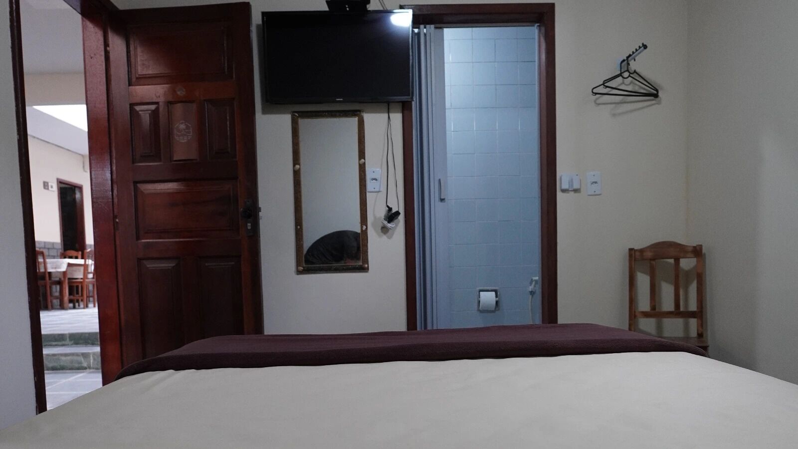 A bedroom with a bed, a TV mounted above a mirror, a door, and a small wooden chair.