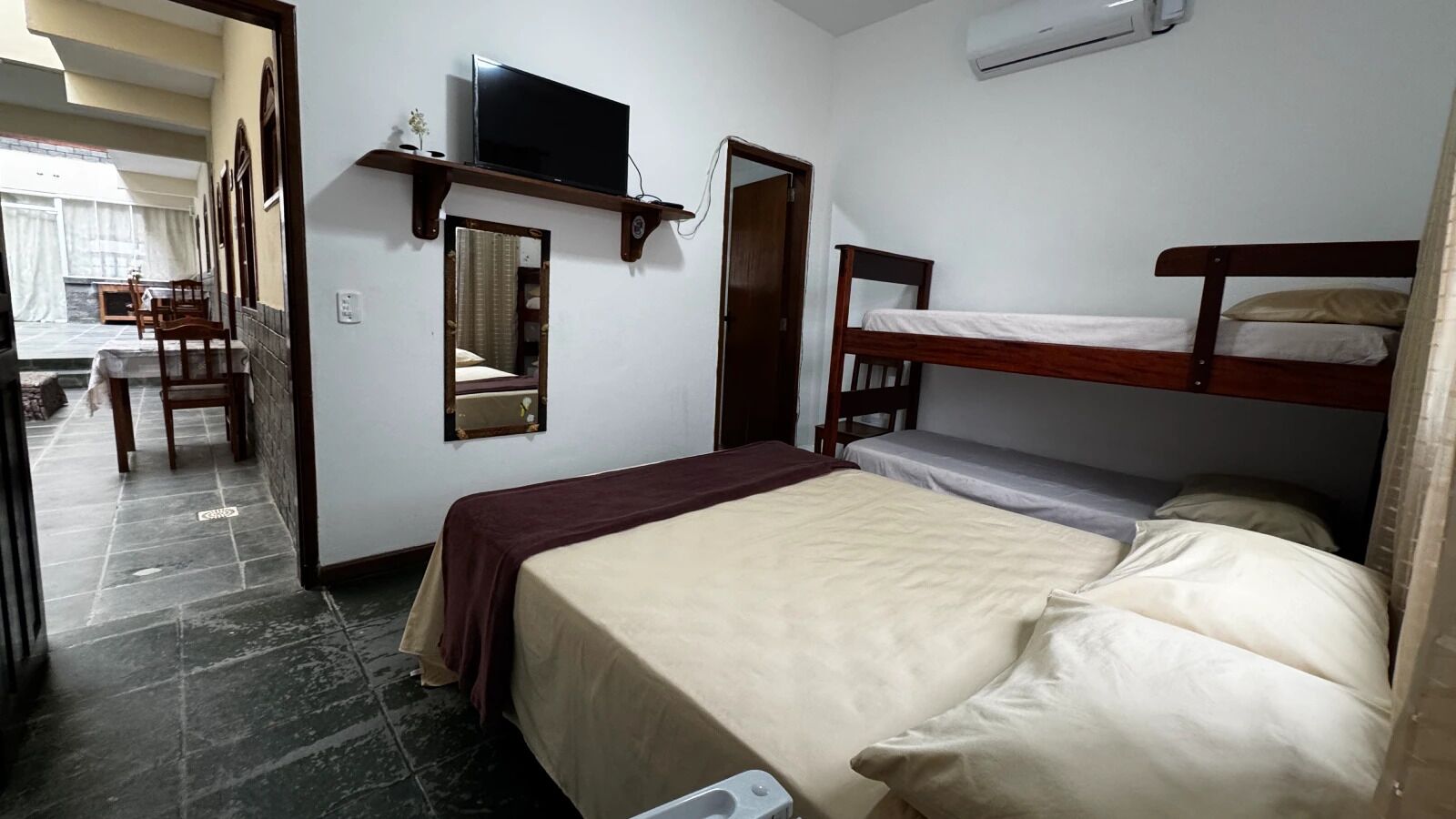 Een hotelkamer met een eenpersoonsbed, een aan een houten plank bevestigde televisie, een spiegel en een kleine tafel met stoelen.