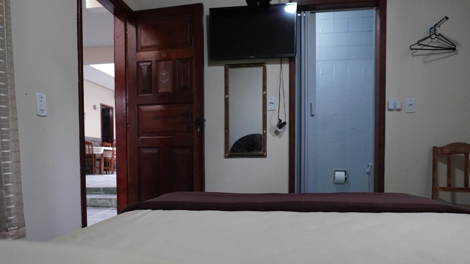 A bedroom with a bed, a wooden door, a mirror, a television, and a clothes hanger.