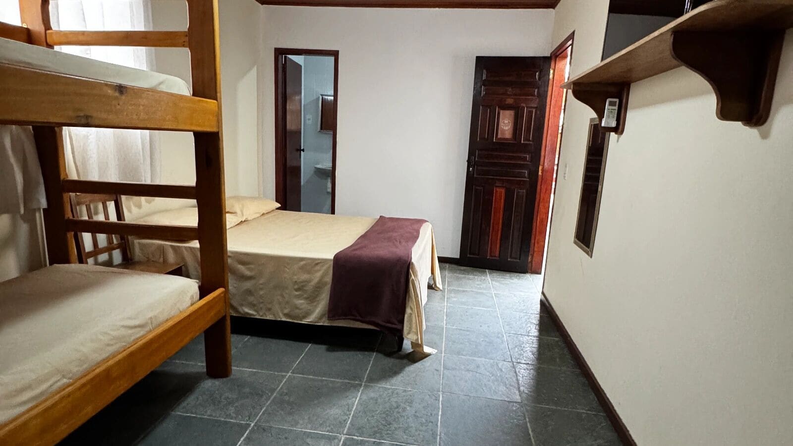 Una habitació amb una llitera, un llit individual i una porta que dona a una altra habitació.