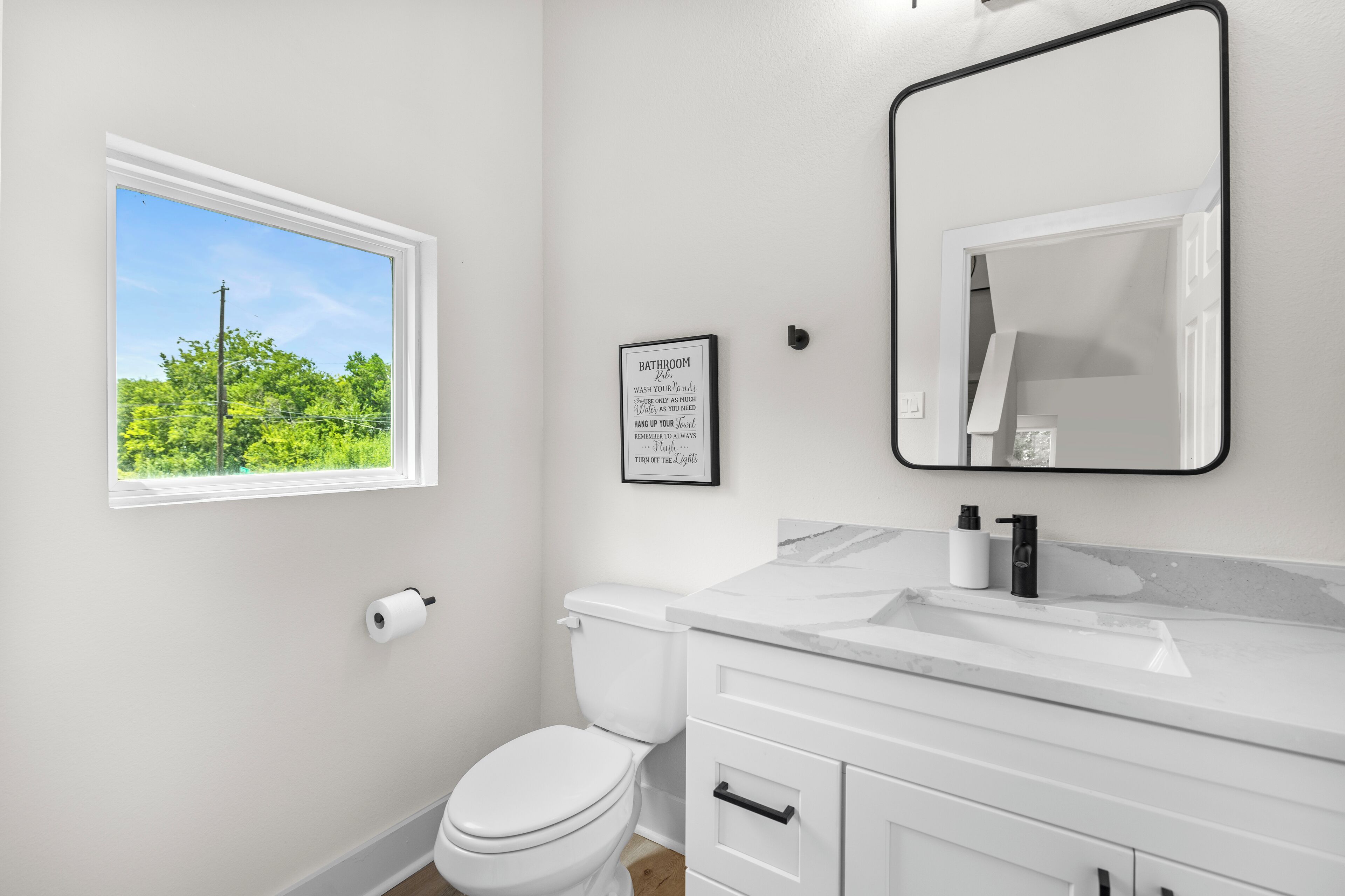 Ein Badezimmer mit Toilette, Waschbecken, Spiegel und einem Fenster mit Blick auf Grünflächen.