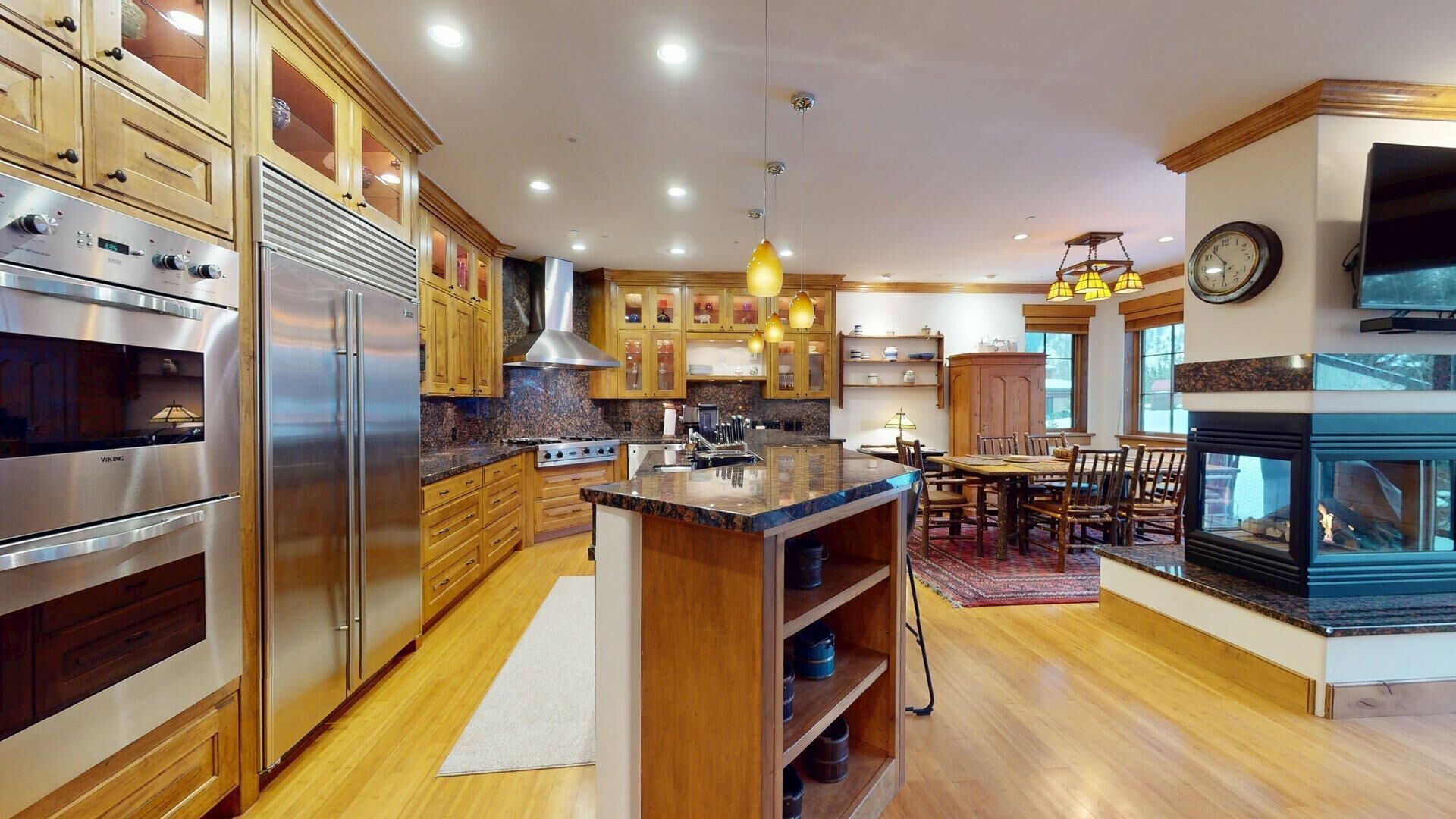 A modern kitchen with wooden cabinets, stainless steel appliances, a central island, pendant lighting, and a built-in fireplace.