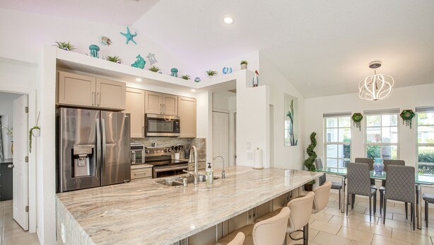 A modern kitchen with a marble countertop, stainless steel appliances, and a bar area with seating. - Heated Saltwater Pool! Family Port Charlotte Home (Port Charlotte)