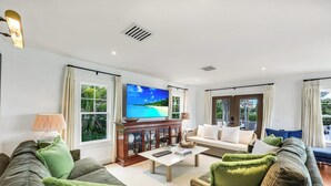 A spacious living room with a large flat-screen TV, comfortable seating, and large windows offering a view of the outdoors. - Royal Harbor - Private Pool (Naples)