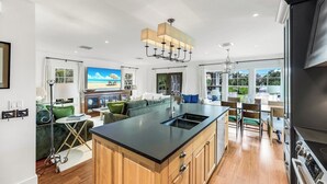 A modern kitchen with a central island, wooden cabinets, and a large window offering a view of the outdoors. - Royal Harbor - Private Pool (Naples)