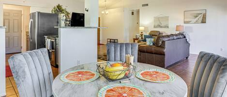 A modern living room with a marble coffee table, grey upholstered chairs, and a dining area with a glass-top table.